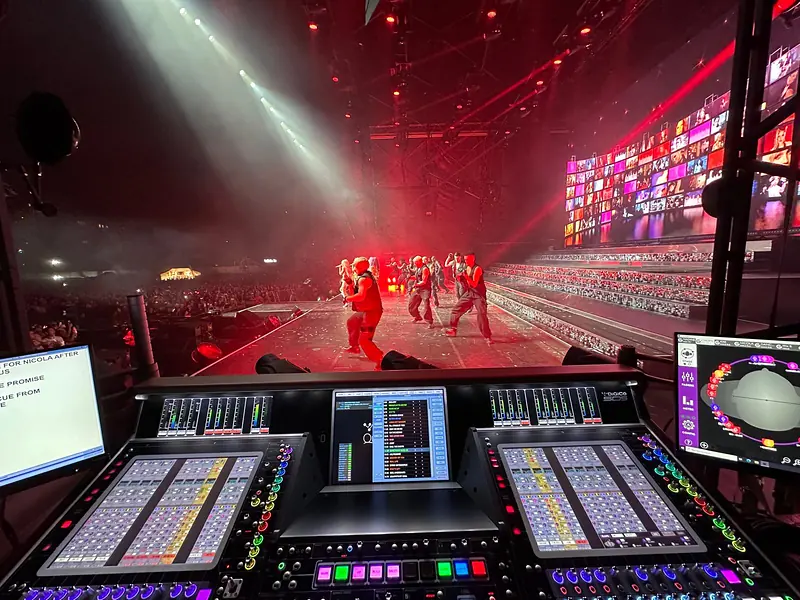 DiGiCo SD5 console at Front of House with dancers and a video wall on stage under red lighting