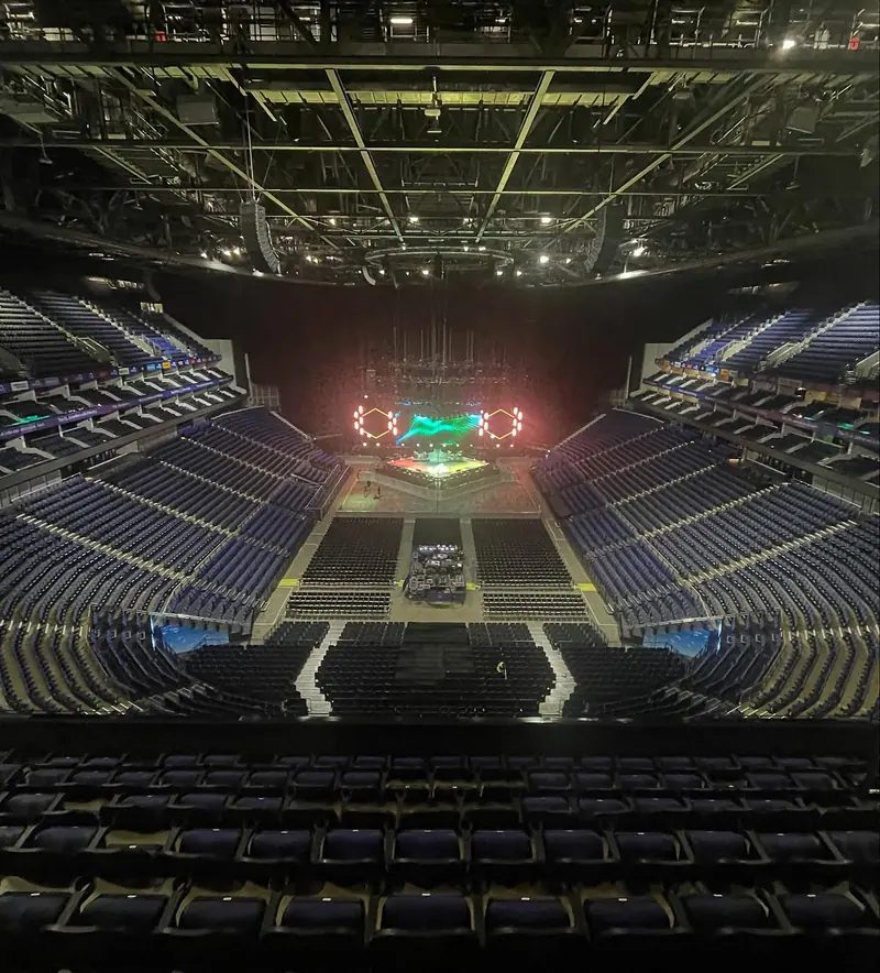 Empty arena seen from the upper tier before the show, with the stage and video screens lit at the far end